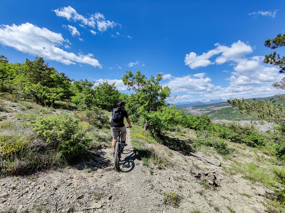 Vttiste sur un sentier des Terres Noires  Digne-les-Bains, entour de vgtation et avec vue sur les montagnes des Alpes-de-Haute-Provence sous un ciel bleu